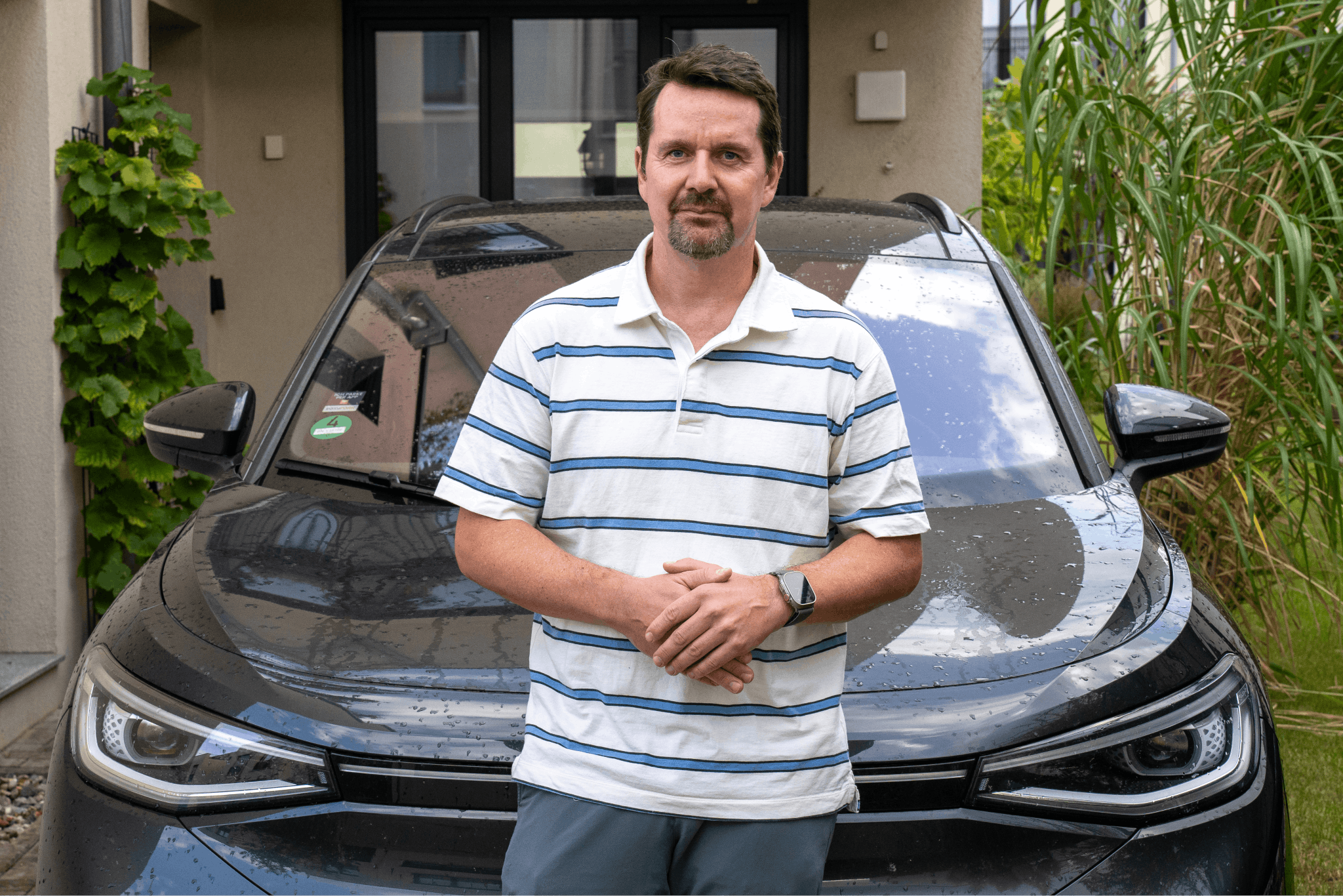 Kunde steht vor seinem Haus und E-Auto