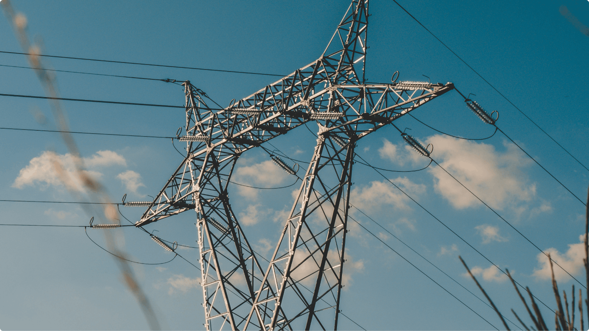Hoogspanningsmast met elektriciteitsdraden tegen een blauwe lucht met lichte bewolking