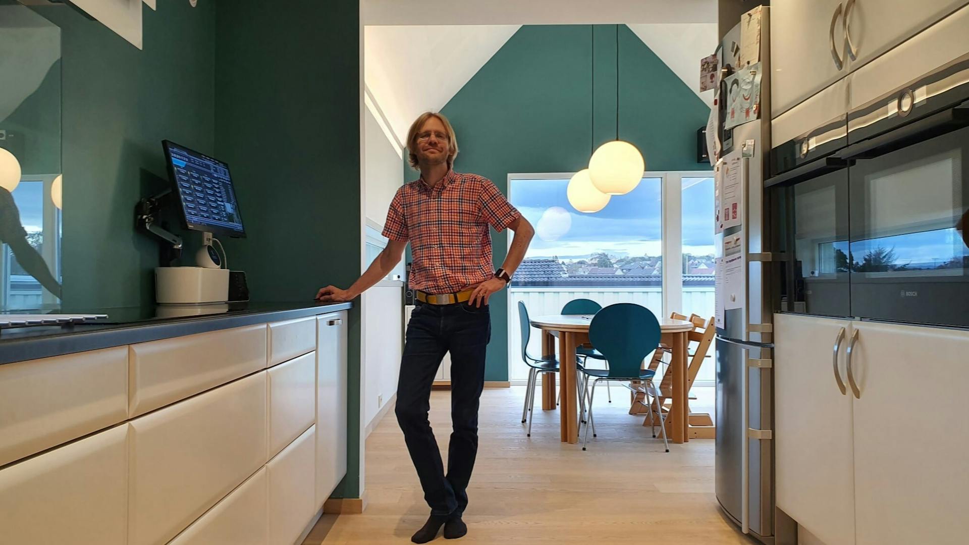 Magnus Ognedal in his kitchen standing next to his board computer with his dining table in the background